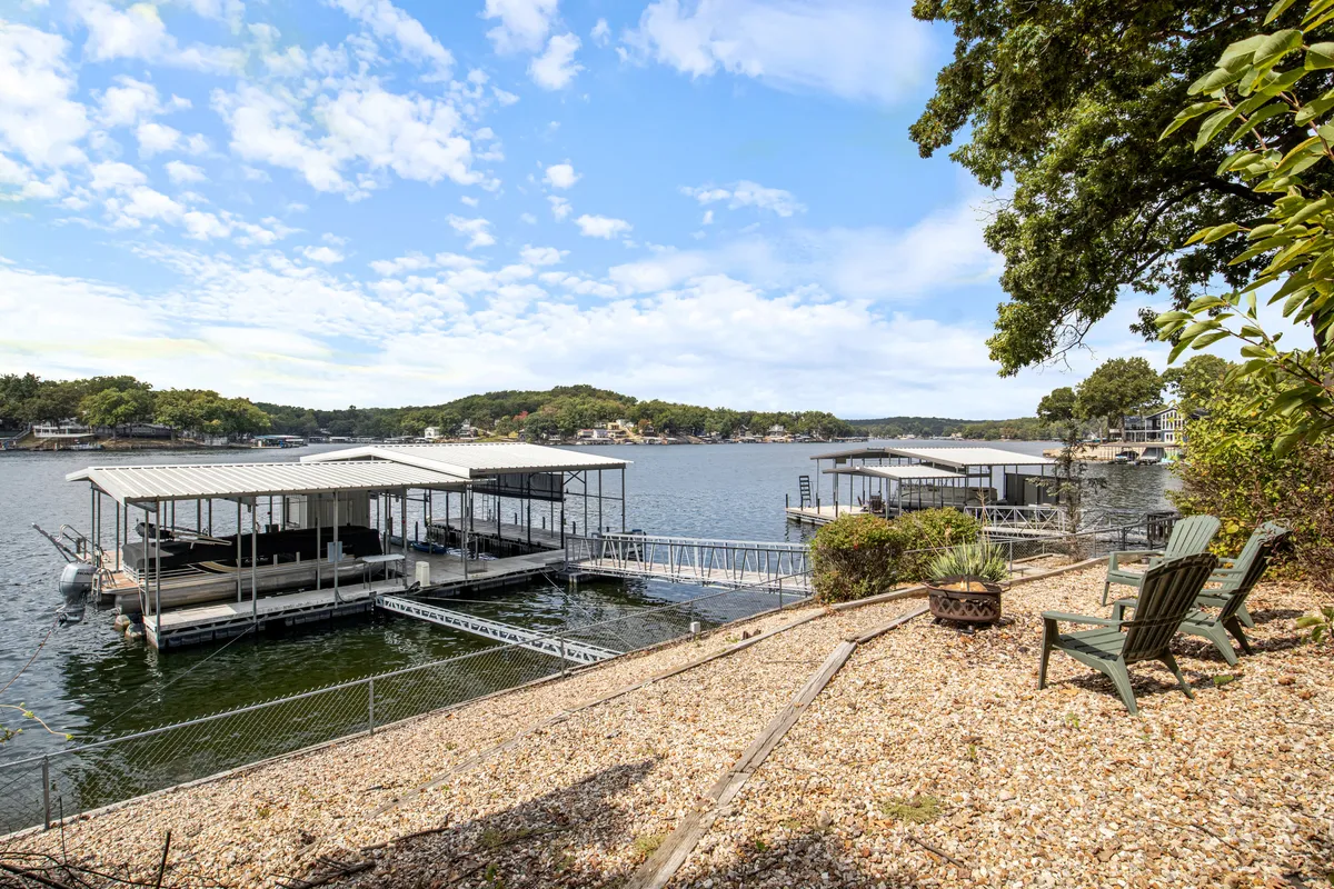 This image provides a tranquil exterior perspective with a focus on the lake, neighboring boathouses, and a comfortable seating area by the water. The composition highlights the peaceful setting, perfect for sunset toasts or quiet moments after active lake adventures.