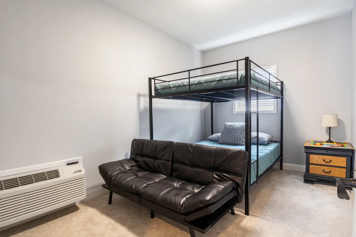 A playful bunk room setup with a sturdy bunk bed, futon, and a nightstand. The casual, inviting vibe is ideal for kids or group sleepovers, with plenty of space for relaxing or reading stories together.