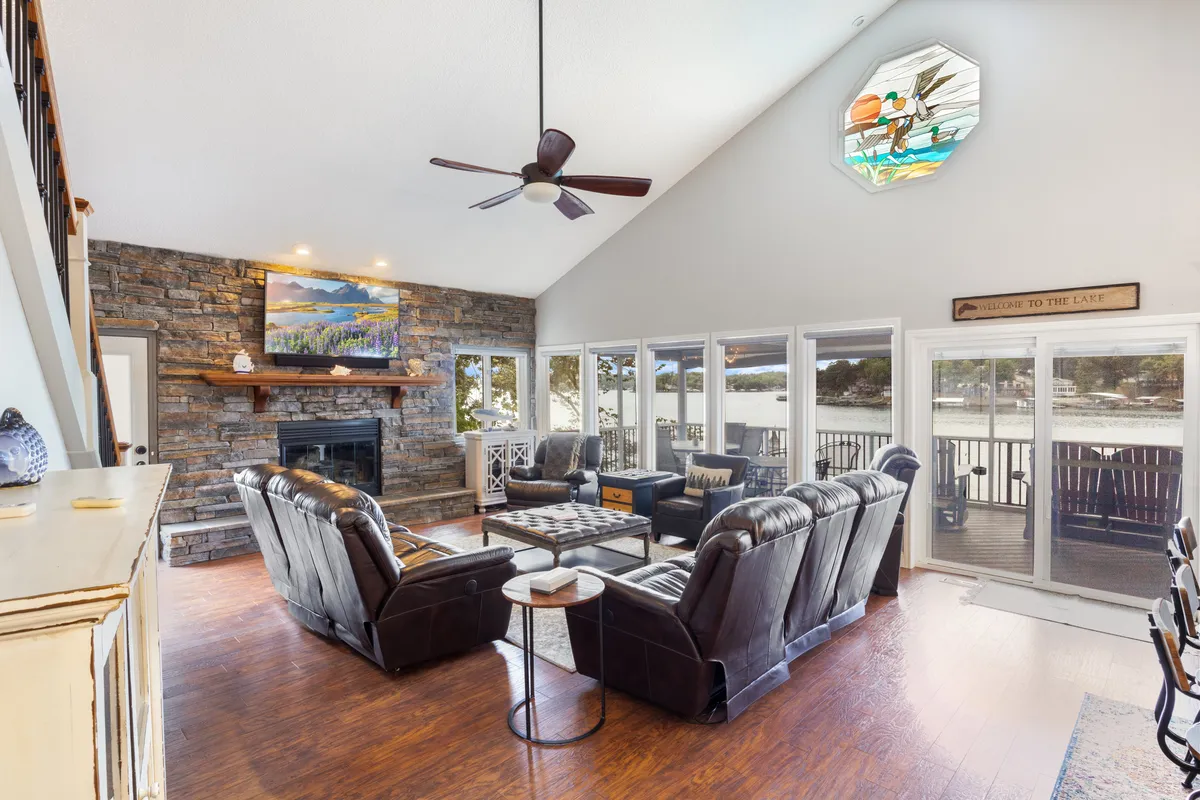 A cozy interior living space with a prominent stone fireplace, large windows letting in natural light, a stained glass feature, and comfortable seating. The view hints at scenic surroundings, while the space invites gathering and planning local outings.