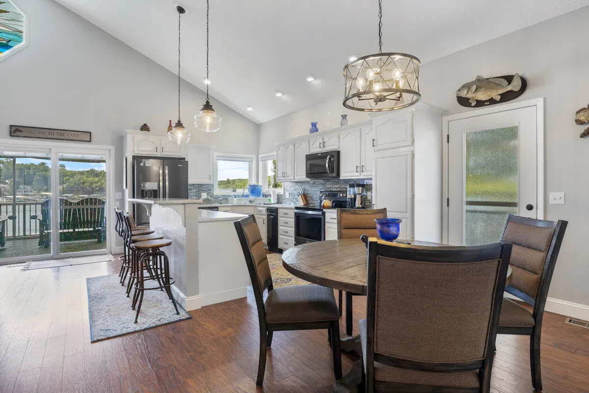 A bright, modern kitchen featuring a central island with bar seating, a spacious dining table, stainless steel appliances, and decorative accents. Large windows let in ample natural light, creating a welcoming atmosphere for cooking, dining, and socializing.