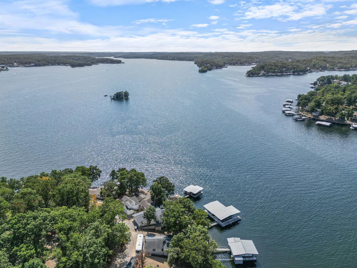 A serene lakeside vista featuring calm water, nearby houses, boats, and tree-lined shores. The spacious dock and tranquil shore invite boating, swimming, picnicking, and other group activities, emphasizing the lakeside context.