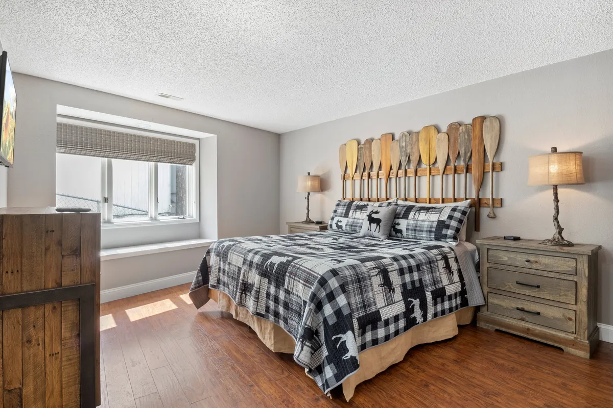 A cozy bedroom featuring a bed with patterned bedding, wooden paddle decor on the wall, and nightstands with ambient lamps. Natural light streams through the window, creating a peaceful and inviting environment.