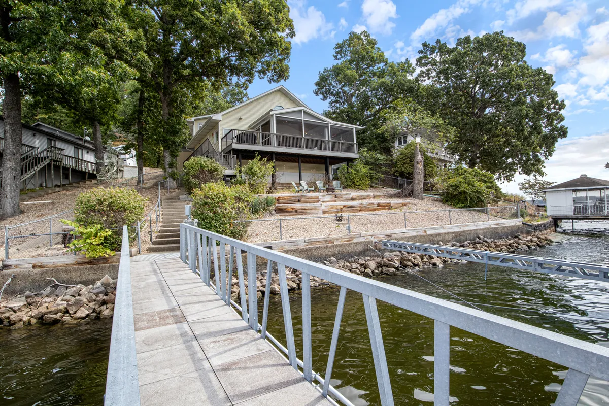 A wide view of the property showcasing the house, a dock extending over the water, and lush landscaping. The scene suggests easy access to lakefront activities and nature walks, with a fully fenced yard visible for added peace of mind.