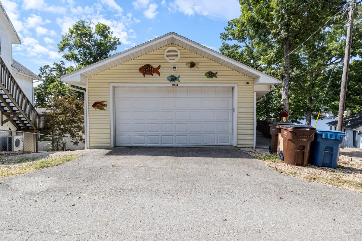 An exterior scene featuring a garage door adorned with decorative fish, surrounded by lush trees and a driveway leading up to the home. The welcoming entrance and outdoor ambiance suggest opportunities for exploration, arrival, and the start of local adventures.