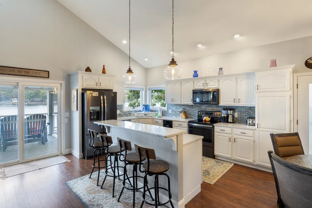 A warm, inviting kitchen with a central island featuring bar seating, modern stainless appliances, elegant cabinetry, and expansive windows framing sunset views. The layout promotes easy conversation and togetherness during meal prep and celebrations.