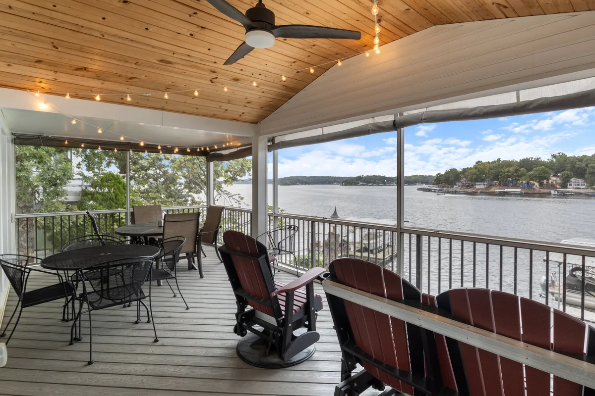 The exterior shows a spacious screened porch outfitted with rocking chairs and a dining table, all overlooking a tranquil lake. String lights add ambiance, making the space ideal for lakeside conversations, al fresco meals, or stargazing.