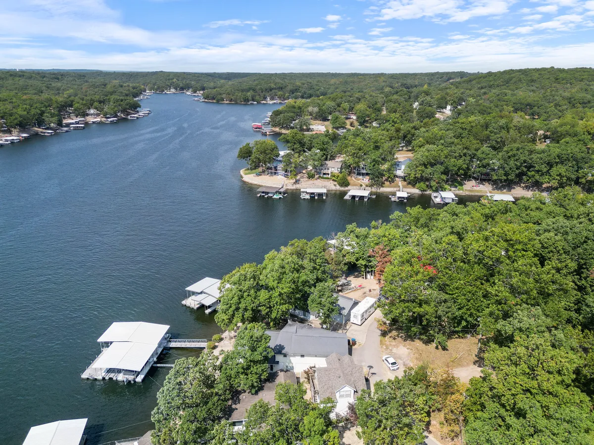 A wide view of the lake with docks, boathouses, and lush trees along the shore. The relaxed mood and open space evoke the spirit of outdoor adventure and community gathering.